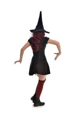 tam uzunlukta portresi kırmızı saçlı kız kara cadı kostüm ve sivri şapka giyiyor. arka beyaz stüdyo arka plan üzerinde izole kamera ile ayakta poz.