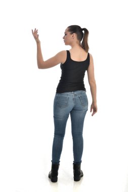 Tam boy siyah tek ve kot giyen esmer kız portresi. geri kamera için ayakta poz. beyaz stüdyo arka plan üzerinde izole.