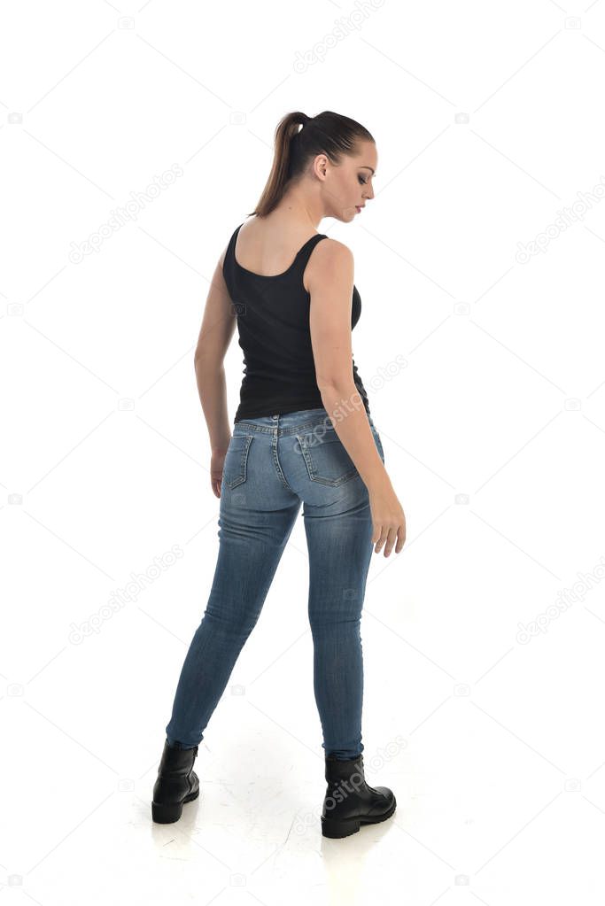 full length portrait of brunette girl wearing black single and jeans. standing pose, back to the camera. isolated on white studio background.
