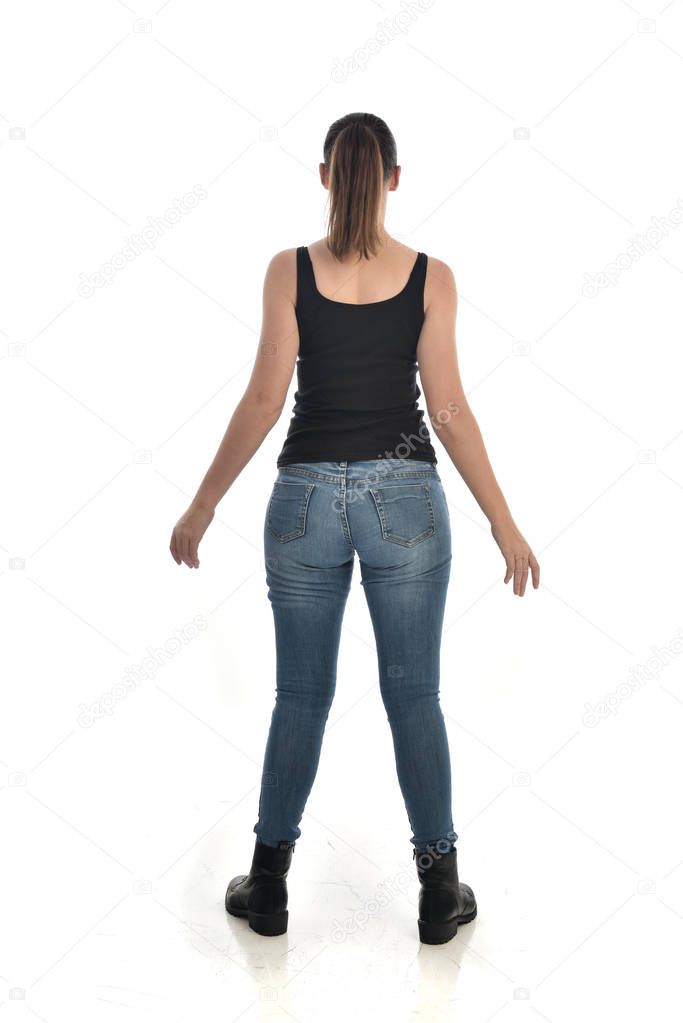 full length portrait of brunette girl wearing black single and jeans. standing pose, back to the camera. isolated on white studio background.