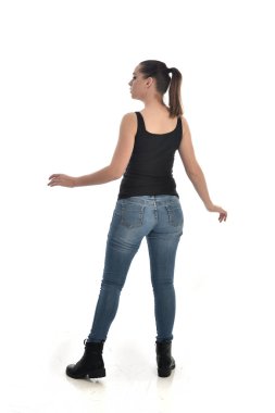 Tam boy siyah tek ve kot giyen esmer kız portresi. geri kamera için ayakta poz. beyaz stüdyo arka plan üzerinde izole.