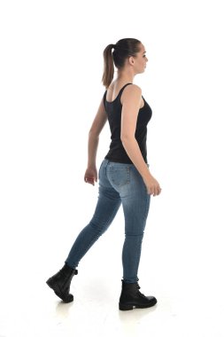 Tam boy siyah tek ve kot giyen esmer kız portresi. geri kamera için ayakta poz. beyaz stüdyo arka plan üzerinde izole.