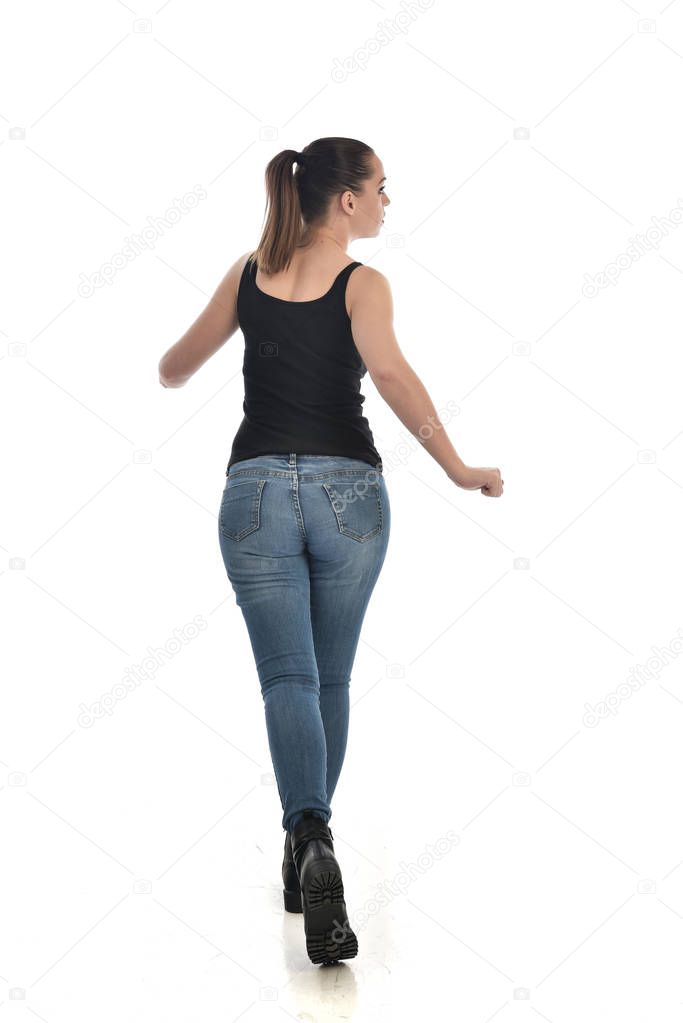 full length portrait of brunette girl wearing black single and jeans. standing pose, back to the camera. isolated on white studio background.