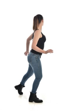 Tam boy siyah tek ve kot giyen esmer kız portresi. geri kamera için ayakta poz. beyaz stüdyo arka plan üzerinde izole.