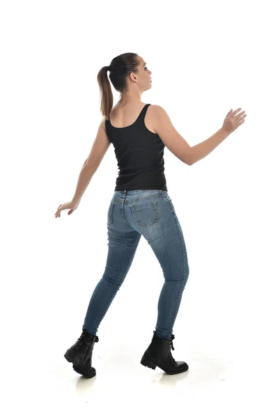 黒シングルとジーンズを身に着けているブルネットの女の子の完全な長さの肖像画 立ちポーズ カメラに戻る ホワイト スタジオの背景に分離 — ストック写真