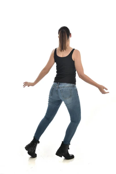 黒シングルとジーンズを身に着けているブルネットの女の子の完全な長さの肖像画 立ちポーズ カメラに戻る ホワイト スタジオの背景に分離 — ストック写真