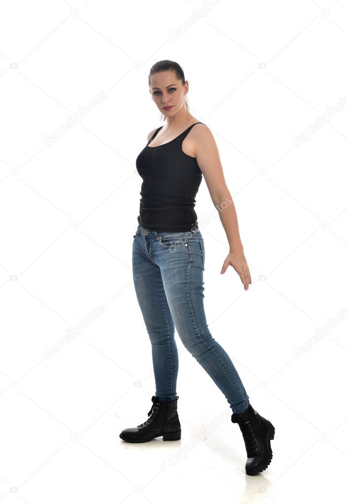 full length portrait of brunette girl wearing black single and jeans. standing pose. isolated on white studio background.