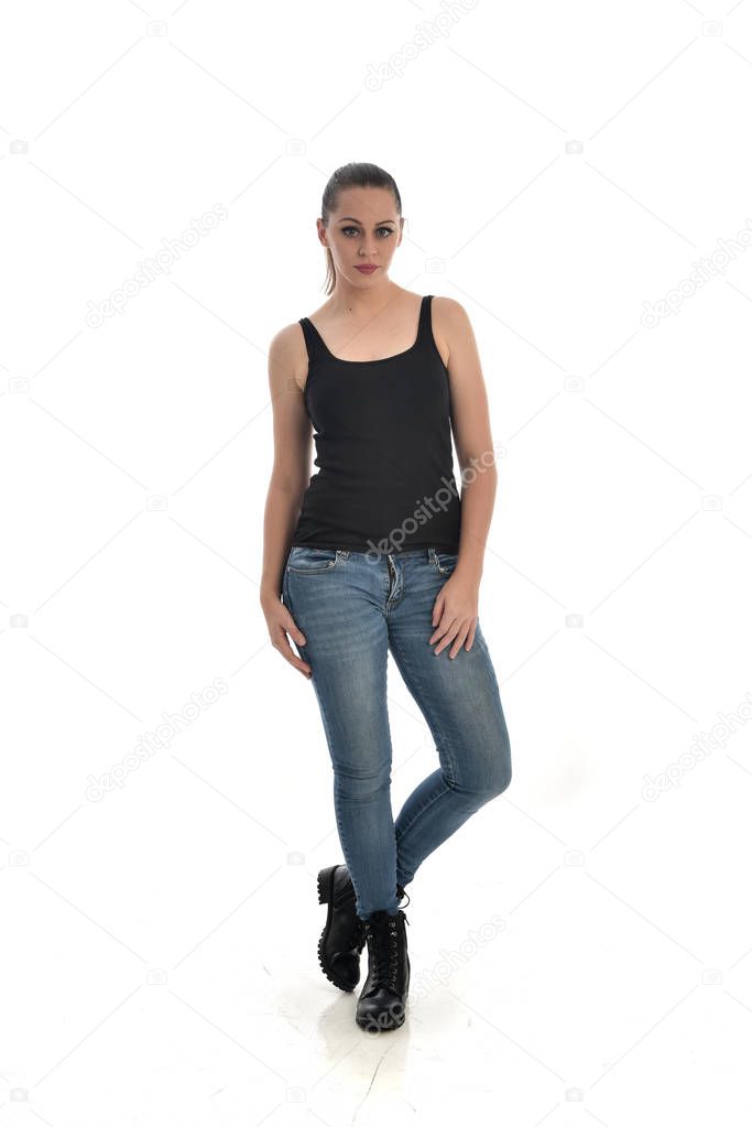 full length portrait of brunette girl wearing black single and jeans. standing pose. isolated on white studio background.