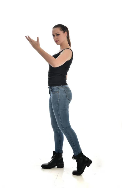 黒シングルとジーンズを身に着けているブルネットの女の子の完全な長さの肖像画 立ちポーズ ホワイト スタジオの背景に分離 — ストック写真