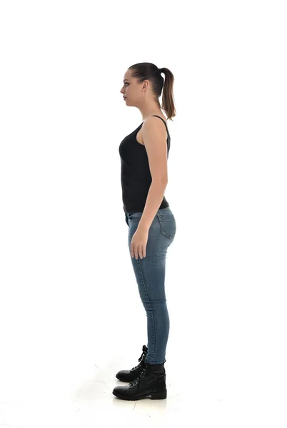 黒シングルとジーンズを身に着けているブルネットの女の子の完全な長さの肖像画 立ちポーズ ホワイト スタジオの背景に分離 — ストック写真