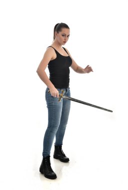 Tam boy siyah tek ve kot giyen esmer kız portresi. bir kılıç holding ayakta poz. beyaz stüdyo arka plan üzerinde izole.