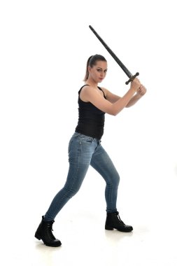 Tam boy siyah tek ve kot giyen esmer kız portresi. bir kılıç holding ayakta poz. beyaz stüdyo arka plan üzerinde izole.