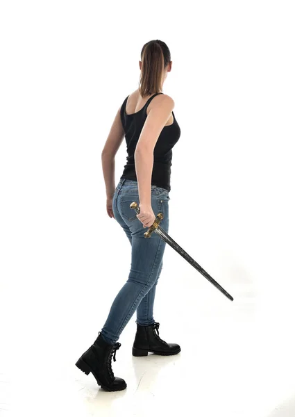 黒シングルとジーンズを身に着けているブルネットの女の子の完全な長さの肖像画 立ちポーズ 剣を保持しています ホワイト スタジオの背景に分離 — ストック写真