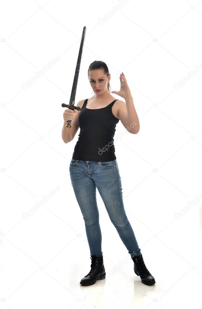 full length portrait of brunette girl wearing black single and jeans. standing pose, holding a sword. isolated on white studio background.