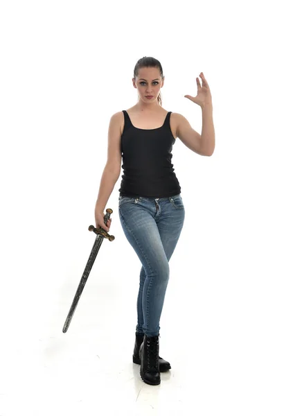 穿黑色单和牛仔裤的黑发女孩的全长肖像 站立姿势 拿着一把剑 在白色工作室背景下被隔离 — 图库照片