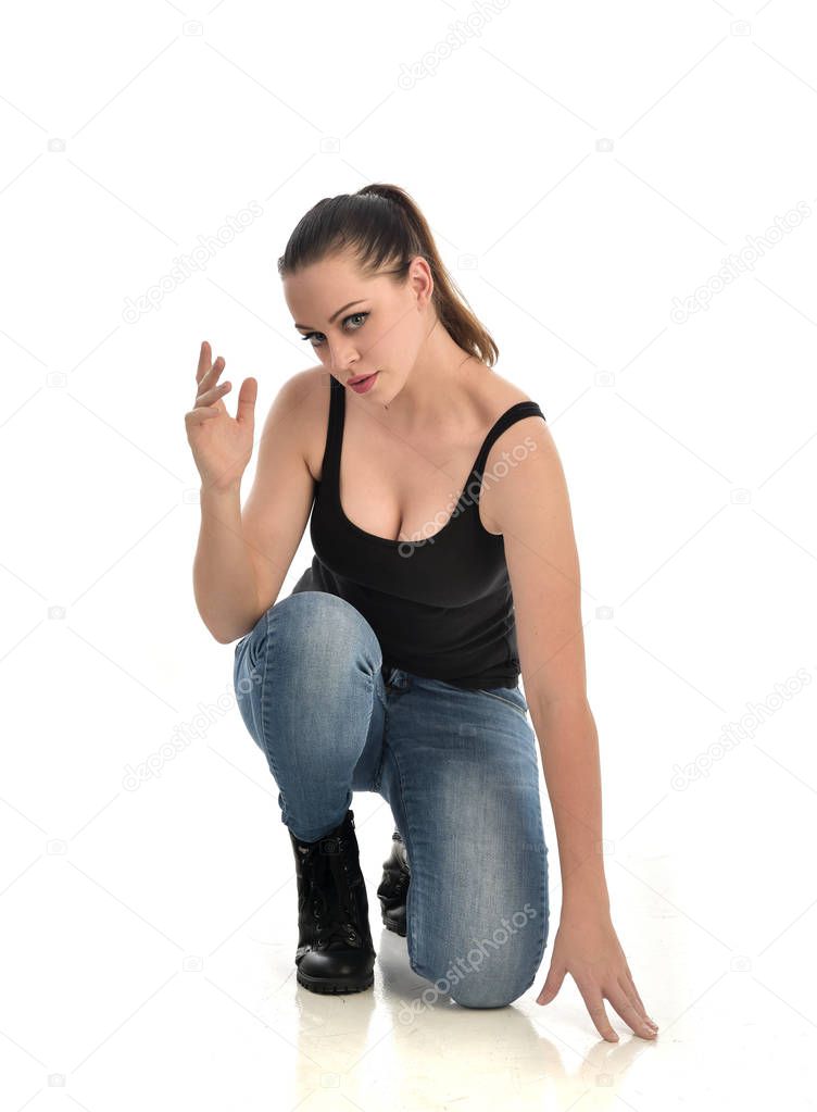 full length portrait of brunette girl wearing black single and jeans. seated pose. isolated on white studio background.