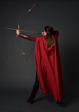 Tam boy esmer kız kırmızı Ortaçağ kostüm ve pelerin, ok ve yay tutarak portresi. gri studio arka plan üzerinde ayakta poz.