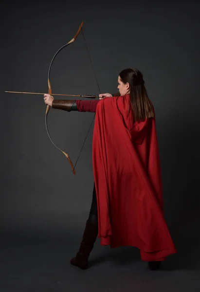 身穿红色中世纪服装和斗篷的黑发女孩全长肖像 手持弓和箭 在灰色演播室背景站立的姿势 — 图库照片