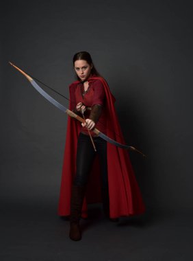 Tam boy esmer kız kırmızı Ortaçağ kostüm ve pelerin, ok ve yay tutarak portresi. gri studio arka plan üzerinde ayakta poz.