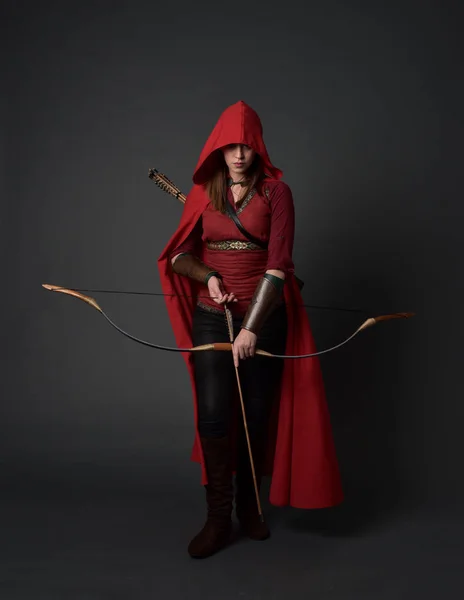 身穿红色中世纪服装和斗篷的黑发女孩全长肖像 手持弓和箭 在灰色演播室背景站立的姿势 — 图库照片