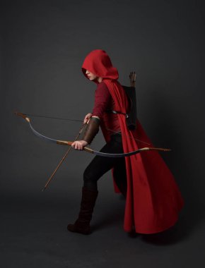 Tam boy esmer kız kırmızı Ortaçağ kostüm ve pelerin, ok ve yay tutarak portresi. gri studio arka plan üzerinde ayakta poz.