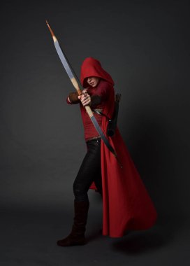 Tam boy esmer kız kırmızı Ortaçağ kostüm ve pelerin, ok ve yay tutarak portresi. gri studio arka plan üzerinde ayakta poz.