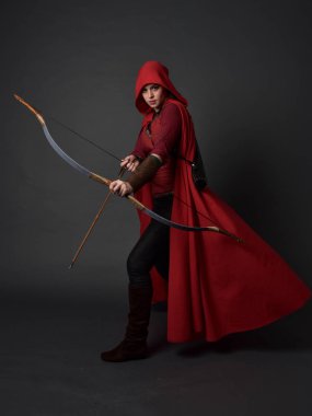 Tam boy esmer kız kırmızı Ortaçağ kostüm ve pelerin, ok ve yay tutarak portresi. gri studio arka plan üzerinde ayakta poz.
