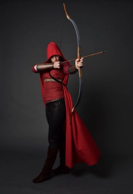 Tam boy esmer kız kırmızı Ortaçağ kostüm ve pelerin, ok ve yay tutarak portresi. gri studio arka plan üzerinde ayakta poz.