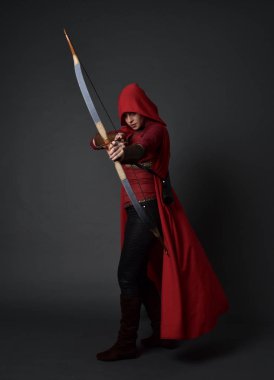 Tam boy esmer kız kırmızı Ortaçağ kostüm ve pelerin, ok ve yay tutarak portresi. gri studio arka plan üzerinde ayakta poz.