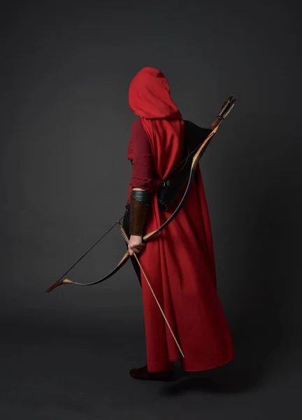 ブルネットの少女レッド中世のコスチュームとマントを身に着けている弓と矢を保持しているの完全な長さの肖像画 灰色のスタジオの背景に立ちポーズ — ストック写真