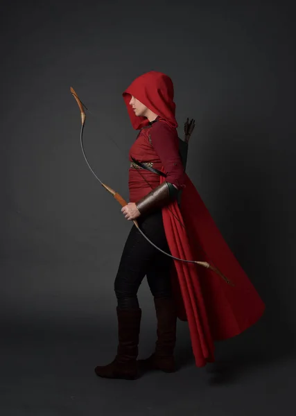 ブルネットの少女レッド中世のコスチュームとマントを身に着けている弓と矢を保持しているの完全な長さの肖像画 灰色のスタジオの背景に立ちポーズ — ストック写真