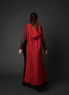 tam uzunlukta kırmızı Ortaçağ kostüm ve pelerin giymiş esmer kız portresi. ayakta poz ile kameranın arkasında gri studio arka plan.