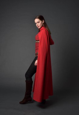 tam uzunlukta kırmızı Ortaçağ kostüm ve pelerin giymiş esmer kız portresi. gri studio arka plan üzerinde ayakta poz.