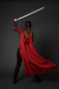 tam uzunlukta kırmızı Ortaçağ kostüm ve pelerin giymiş esmer kız portresi. ayakta poz ile tekrar fotoğraf gri studio arka plan üzerinde bir kılıç holding için.