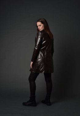 tam uzunlukta uzun deri ceket ve çizmeler giyen esmer kız portresi. ayakta poz ile kameraya gri studio arka arkaya.