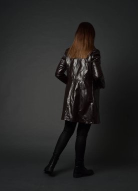 tam uzunlukta uzun deri ceket ve çizmeler giyen esmer kız portresi. ayakta poz ile kameraya gri studio arka arkaya.