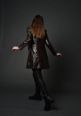 tam uzunlukta uzun deri ceket ve çizmeler giyen esmer kız portresi. ayakta poz ile kameraya gri studio arka arkaya.