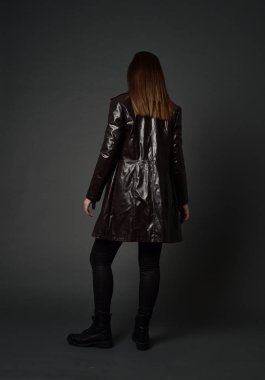 tam uzunlukta uzun deri ceket ve çizmeler giyen esmer kız portresi. ayakta poz ile kameraya gri studio arka arkaya.