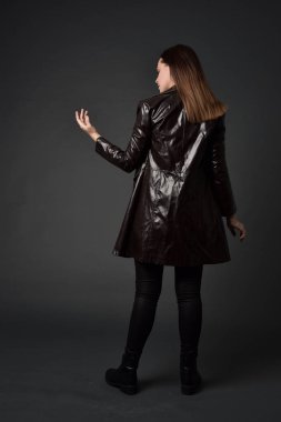 tam uzunlukta uzun deri ceket ve çizmeler giyen esmer kız portresi. ayakta poz ile kameraya gri studio arka arkaya.