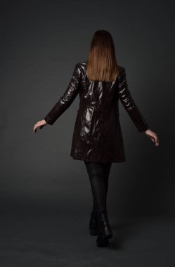 tam uzunlukta uzun deri ceket ve çizmeler giyen esmer kız portresi. ayakta poz ile kameraya gri studio arka arkaya.