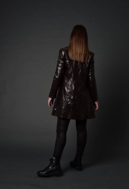 tam uzunlukta uzun deri ceket ve çizmeler giyen esmer kız portresi. ayakta poz ile kameraya gri studio arka arkaya.