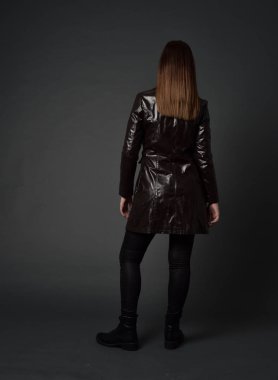 tam uzunlukta uzun deri ceket ve çizmeler giyen esmer kız portresi. ayakta poz ile kameraya gri studio arka arkaya.