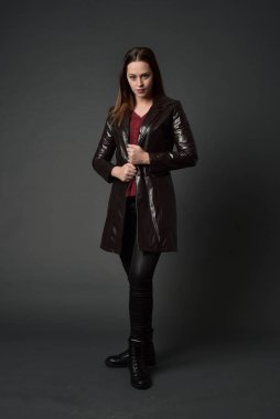 Tam boy esmer kız giyiyor kırmızı uzun deri jack portresi. gri studio arka plan üzerinde ayakta poz.