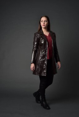 Tam boy esmer kız giyiyor kırmızı uzun deri jack portresi. gri studio arka plan üzerinde ayakta poz.