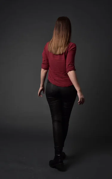 赤いシャツと革のズボンを身に着けているブルネットの女の子の完全な長さの肖像画 灰色のスタジオの背景上の立ちポーズ — ストック写真