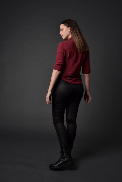 full length portrait of brunette girl wearing  red shirt and leather pants. standing pose , on grey studio background.