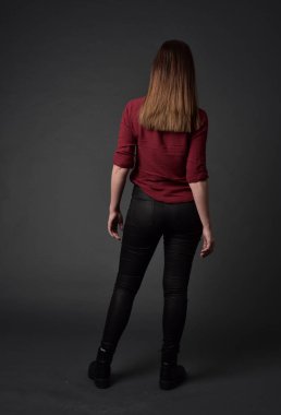 tam uzunlukta kırmızı gömlek ve deri pantolon giyen esmer kız portresi. gri studio arka plan üzerinde ayakta poz.