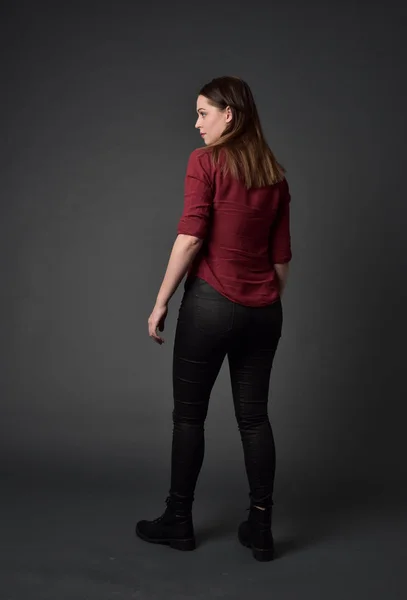 赤いシャツと革のズボンを身に着けているブルネットの女の子の完全な長さの肖像画 灰色のスタジオの背景上の立ちポーズ — ストック写真