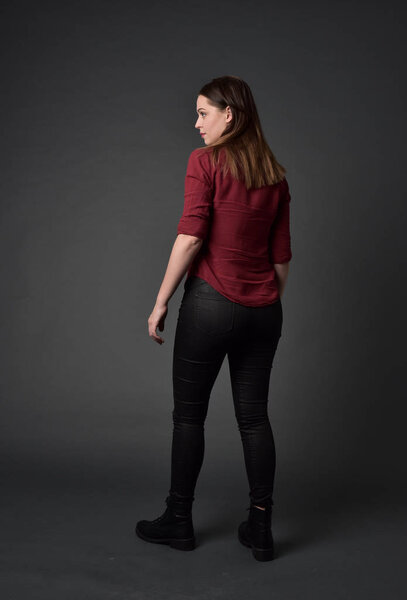 full length portrait of brunette girl wearing  red shirt and leather pants. standing pose , on grey studio background.