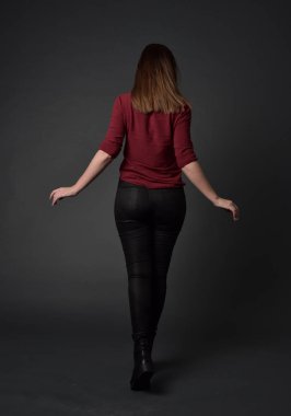 tam uzunlukta kırmızı gömlek ve deri pantolon giyen esmer kız portresi. gri studio arka plan üzerinde ayakta poz.